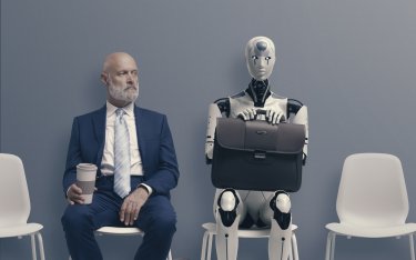 Mann und Roboter sitzen nebeneinander.